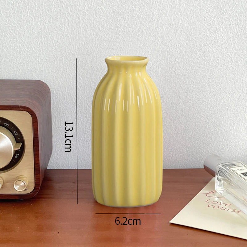 A tall, smooth yellow ceramic bud vase with vertical ridges sits on a wooden surface.