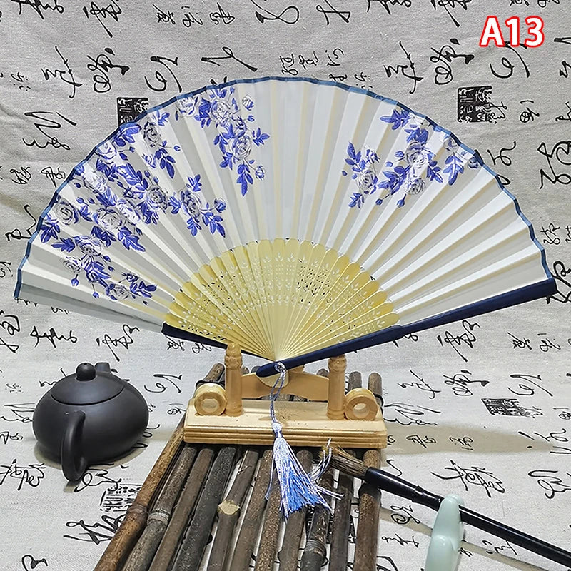An elegant vintage Chinese folding hand fan with blue floral patterns displayed on a wooden stand.