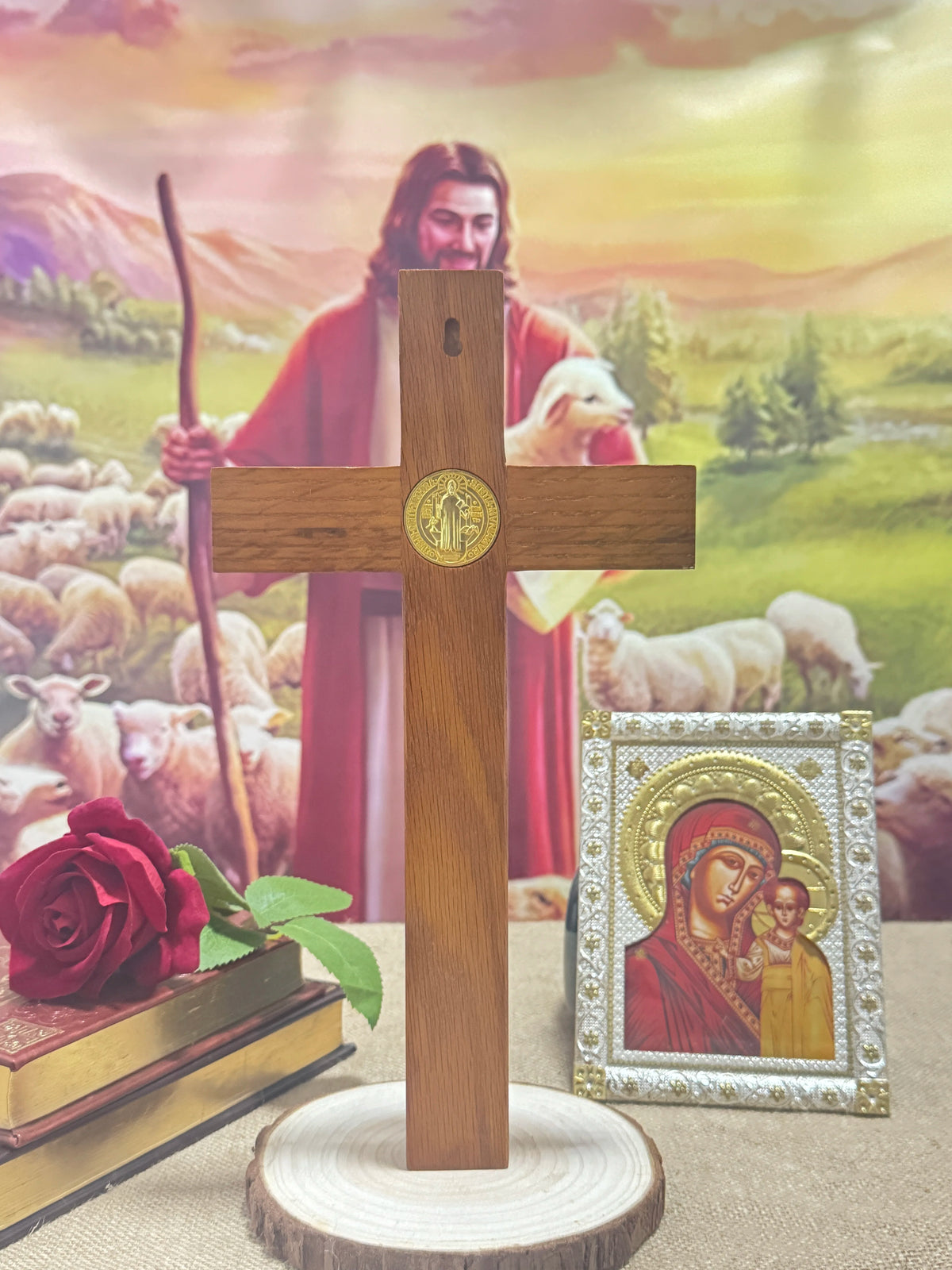 A wooden crucifix with a gold Jesus figure stands on a round base, set against a background of a painting.