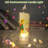 A clear glass candle light featuring a flame-like topper and an etched religious figure, set on a surface with scattered ligh