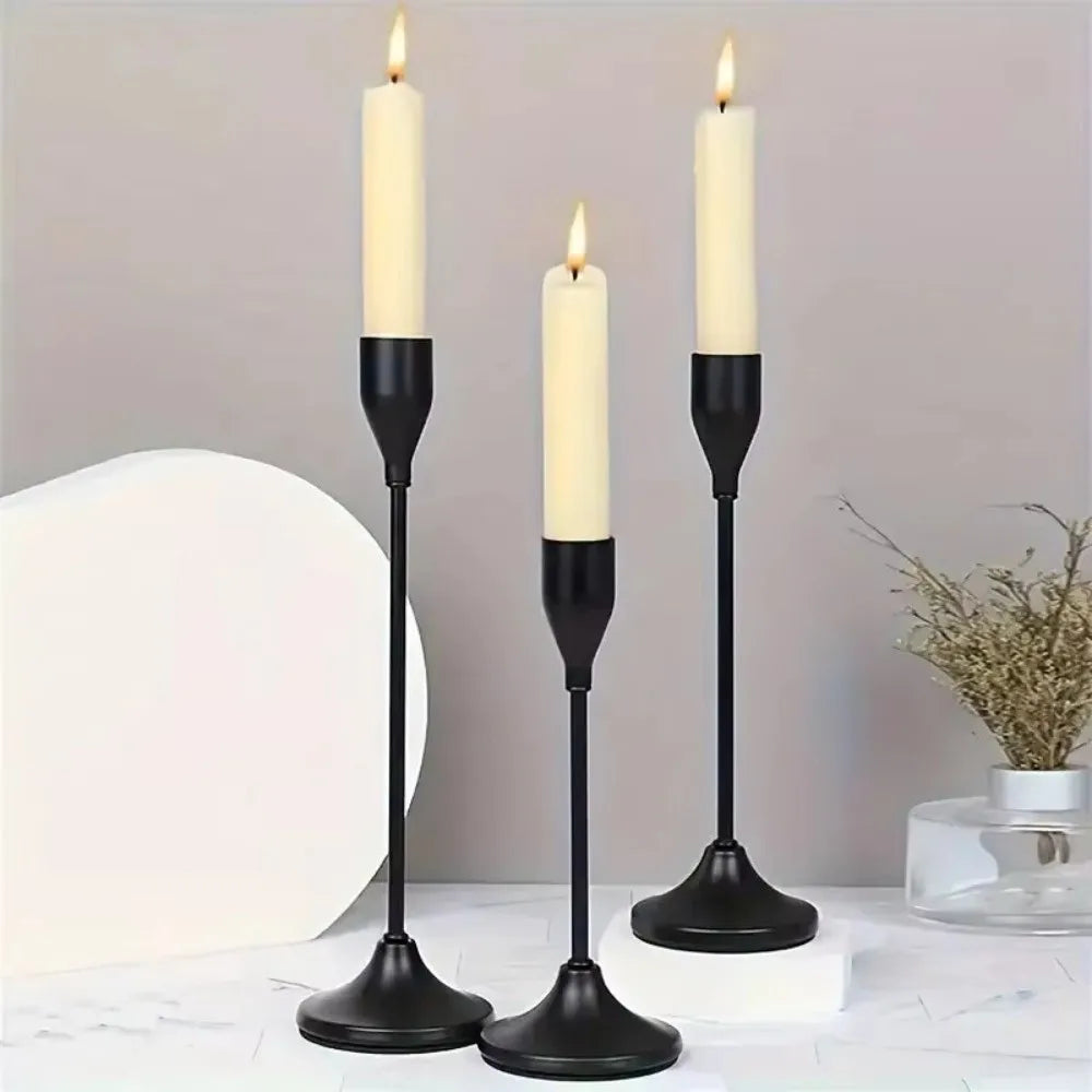 A set of three black minimalist candle holders with white wax candles on a white surface.