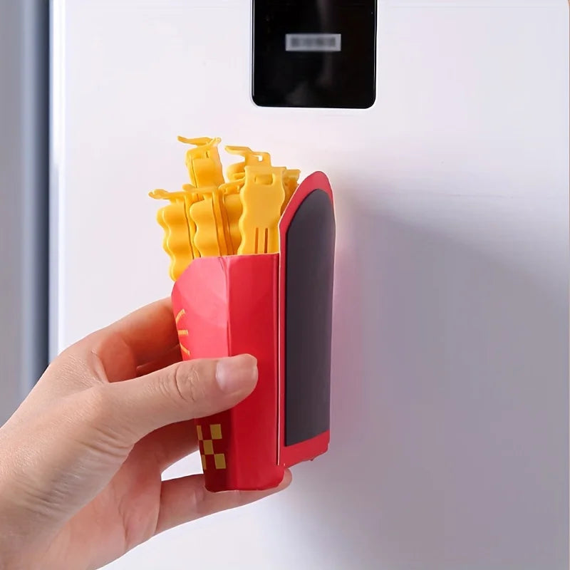 A hand holds a red French fry shaped sealing clip with yellow tips against a white cabinet surface.
