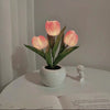 A pink LED tulip night light with petals placed in a white ceramic pot on a table.
