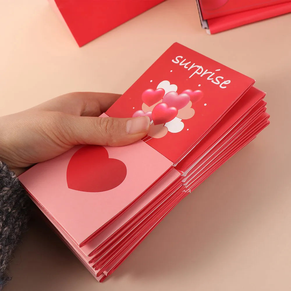 A hand is holding a stack of red cards with the word surprise and heart decorations on them.