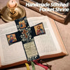 A handmade stitched pocket shrine featuring a cross and religious imagery, resting on an open book.