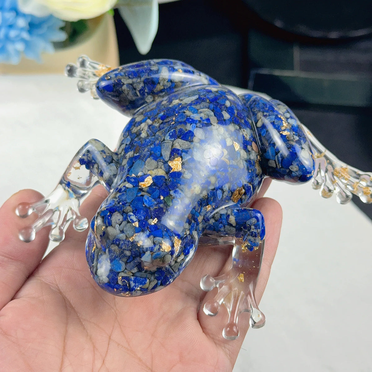 A hand holds a crystal frog resin craft decoration with blue and gold speckles.