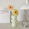 A white ceramic flower vase holding a dried orange-colored flower, next to a list of poem lines.
