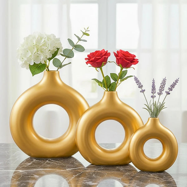 Three gold geometric resin vases holding white and red roses on a marble surface.