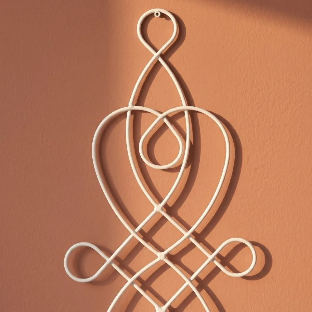 A white decorative iron wall candle sconce set with an intricate, swirling design mounted on a peach-colored wall.
