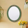 An oval wall mirror with a green frame and intricate lace design hanging on a beige wall.