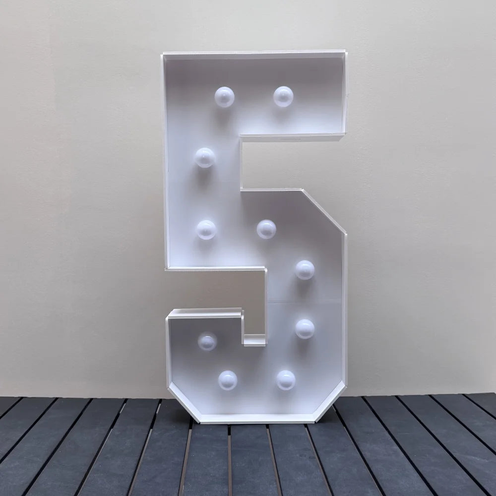 A white marquee number sign shaped like the number 5 with round lights displayed on a dark wooden surface.