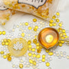 Yellow and clear wax sealing beads scattered on a white surface next to a small gold-colored bowl.