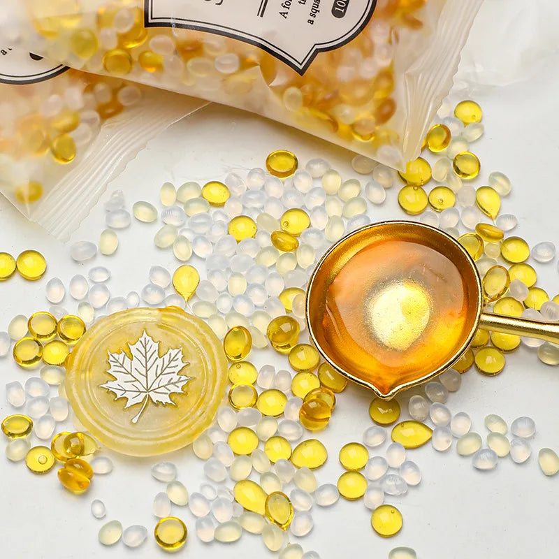 Yellow and clear wax sealing beads scattered on a white surface next to a small gold-colored bowl.