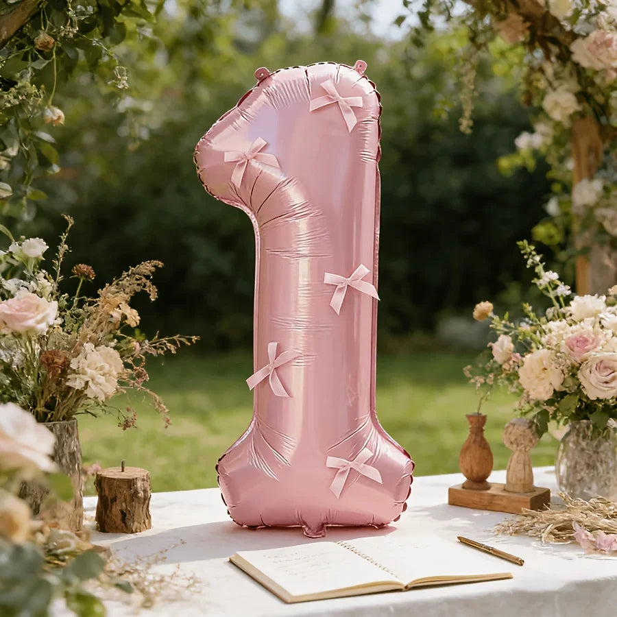 A large pink foil number balloon shaped like the number one stands on a white table surrounded by floral arrangements.