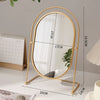 A gold-framed oval vanity mirror with a rotating stand and a natural light background.