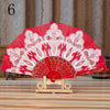 A red lace folding hand fan with white embroidery displayed on a wooden stand.