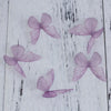 Purple organza butterfly embellishments scattered on a white wooden surface.