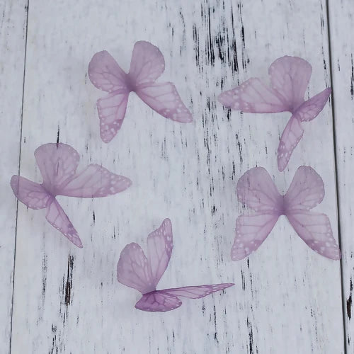 Purple organza butterfly embellishments scattered on a white wooden surface.
