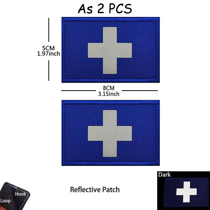 A dark blue reflective patch with a silver cross symbol, measuring 5cm by 8cm.