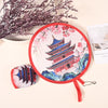 A round fabric hand fan with a red border featuring a detailed illustration of a traditional Chinese pagoda and pink floral p