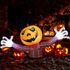 An inflatable orange pumpkin decoration with white arms and a carved face sits on the ground in a dark outdoor setting.