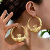 A close-up of a person wearing oversized gold bamboo hoop earrings.