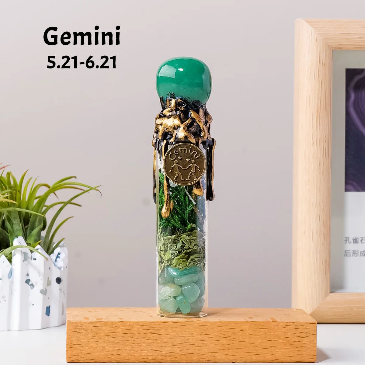 A tall glass bottle filled with green crystals and topped with a green stone, labeled Gemini.