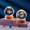 A crystal ball night light with a golden top and dark celestial scene rests on a wooden base.