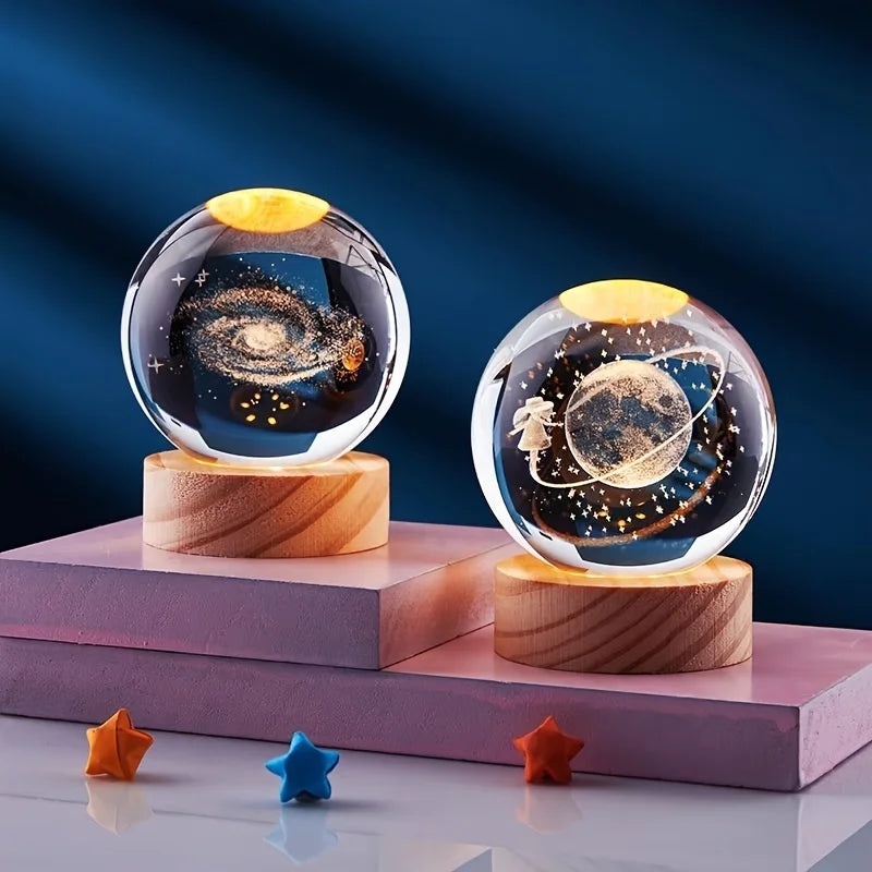 A crystal ball night light with a golden top and dark celestial scene rests on a wooden base.
