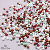 A pile of faceted bicone glass beads in mixed colors including red, green, white, and copper tones.