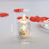 A clear crystal candle in a glass holder with a flickering LED light, surrounded by dried red fruit pieces.