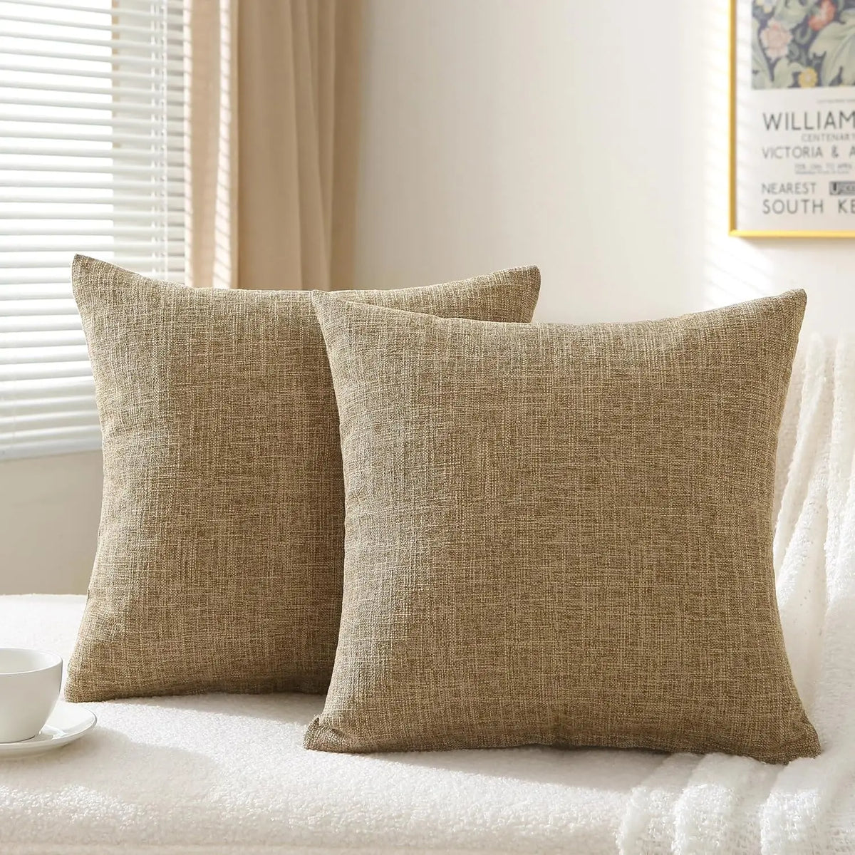 A set of two beige linen pillows resting on a white surface.
