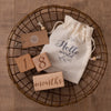 A bundle of wooden baby milestone cards and a natural linen drawstring bag displayed on a woven tray.