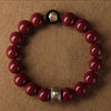 A bracelet made of polished red cinnabar stones and a dark bead, worn on a brown surface.