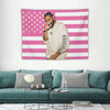 Un homme en chemise claire devant une décoration murale de drapeau américain rayé rose et blanc.