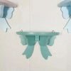 A light blue decorative bow-shaped wooden wall shelf mounted on a white surface.
