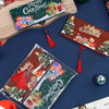A festive cash gift box with Christmas designs and red tassels is displayed on a dark blue surface.