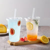 Two clear plastic cups filled with iced beverages, one blue and one orange, garnished with fruit and herbs.