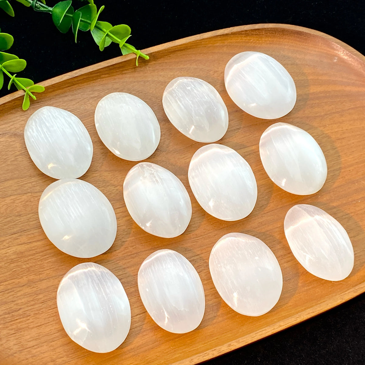 Several smooth, translucent white selenite palm crystals are arranged on a wooden tray.