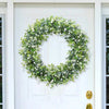 A circular garland of silvery-green eucalyptus leaves adorns a white door.