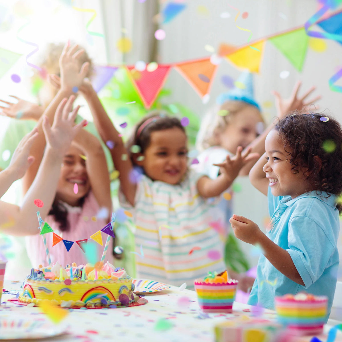 A group of young children celebrating with colorful tissue paper confetti dots and a birthday cake.