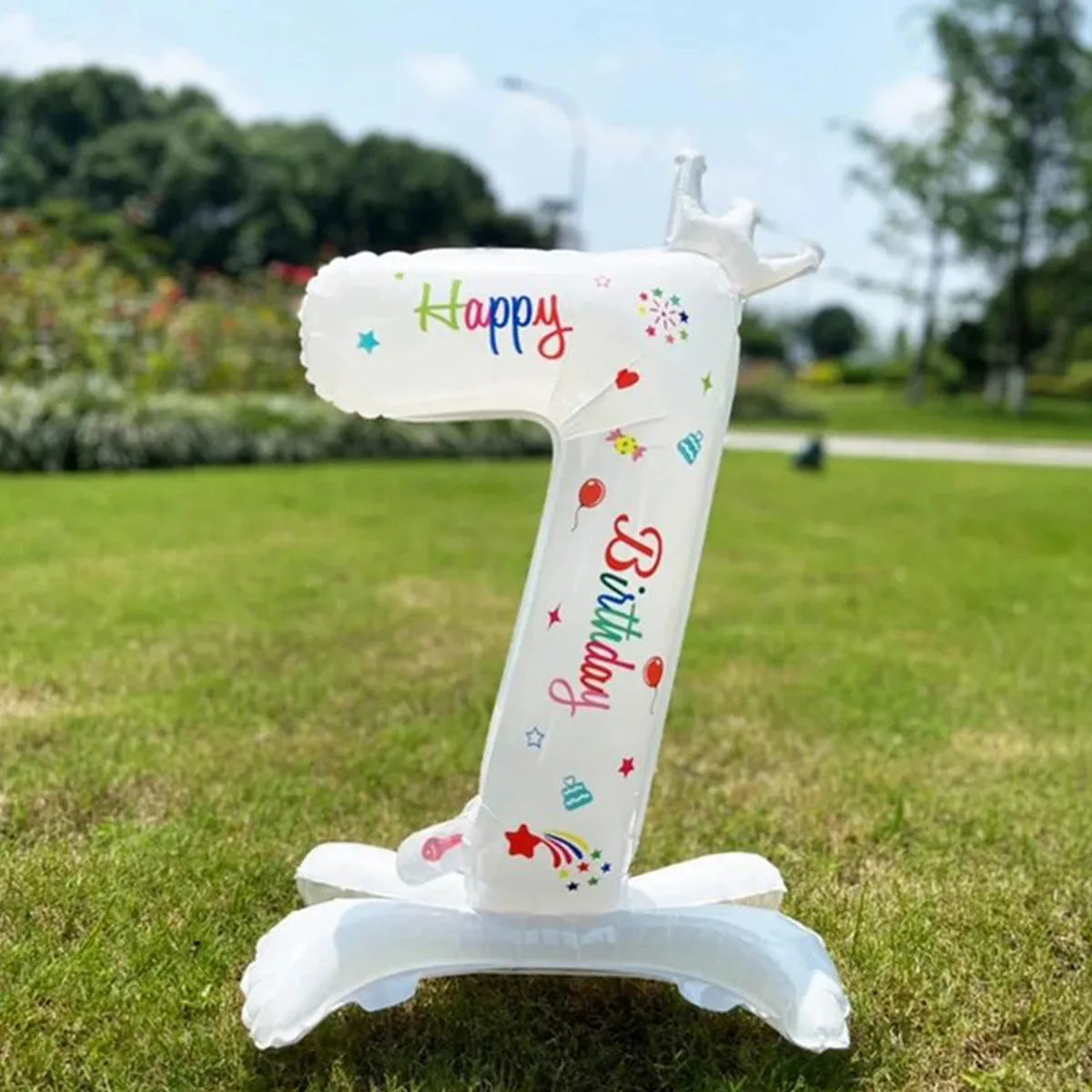 A white standing foil balloon shaped like the number one with a crown and birthday text, placed on green grass.