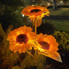 Three glowing orange solar sunflower LED garden lights blooming in a dark garden setting.