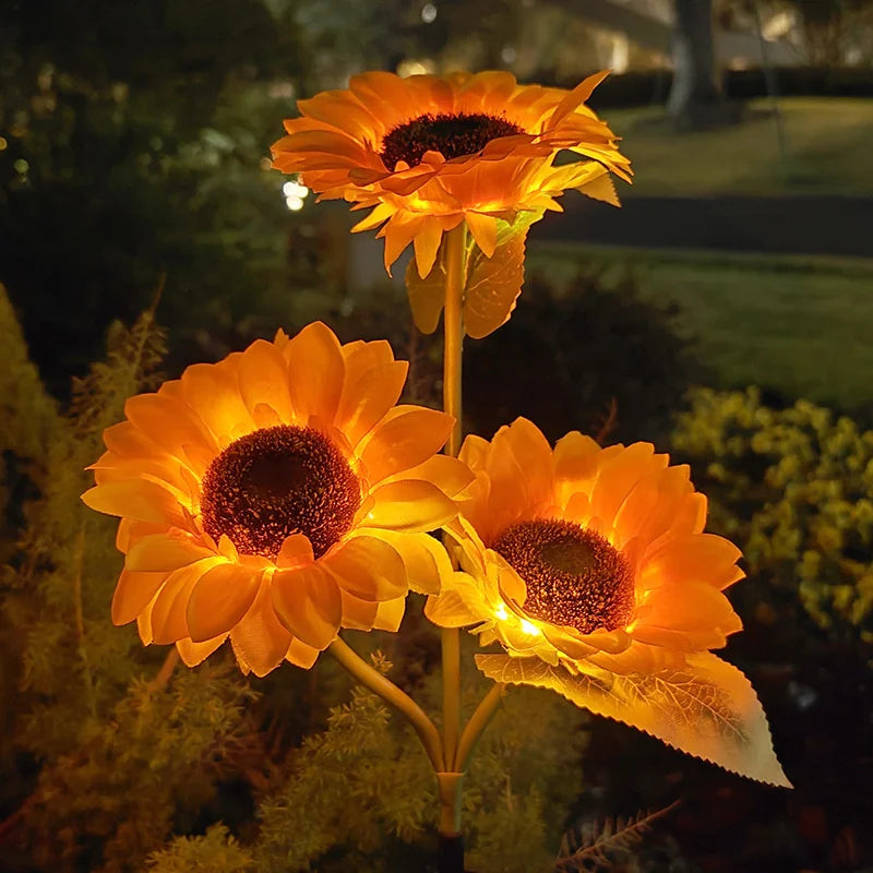Three glowing orange solar sunflower LED garden lights blooming in a dark garden setting.