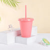 A pink plastic cold cup with a lid and straw is displayed on white blocks.