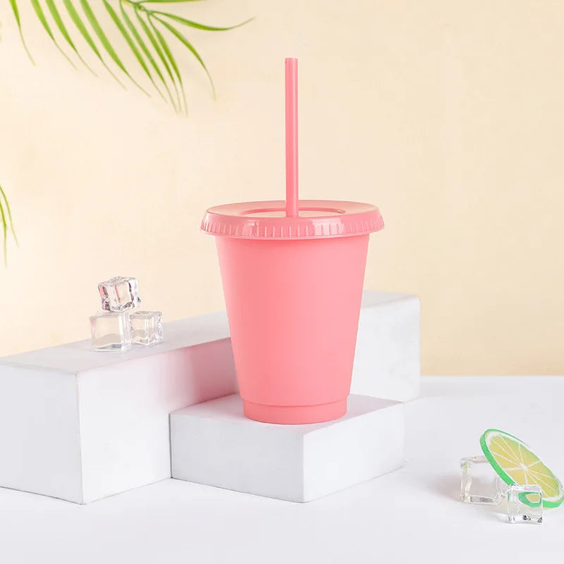 A pink plastic cold cup with a lid and straw is displayed on white blocks.