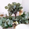 A bouquet of artificial eucalyptus stems with white flowers and green leaves displayed on a table.