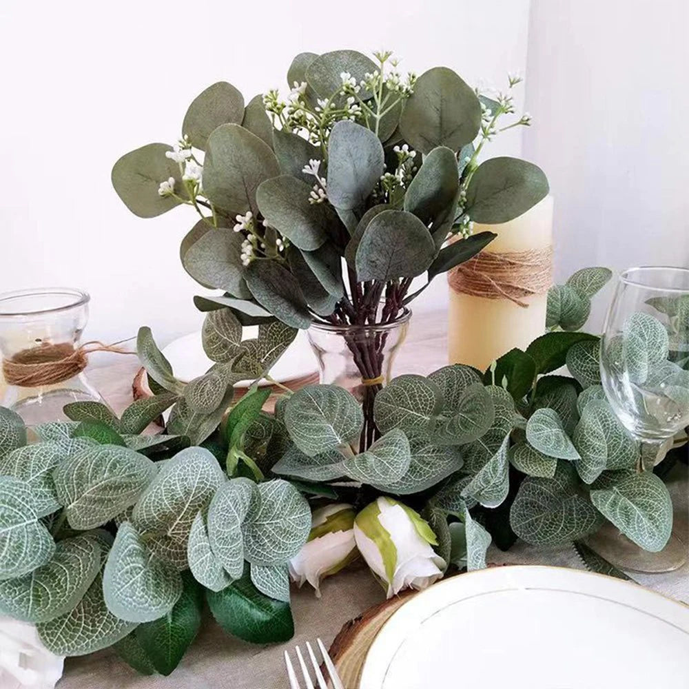 A bouquet of artificial eucalyptus stems with white flowers and green leaves displayed on a table.