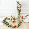A silk rose garland featuring pink and yellow roses draped on a white vase and laid out on a wooden surface.