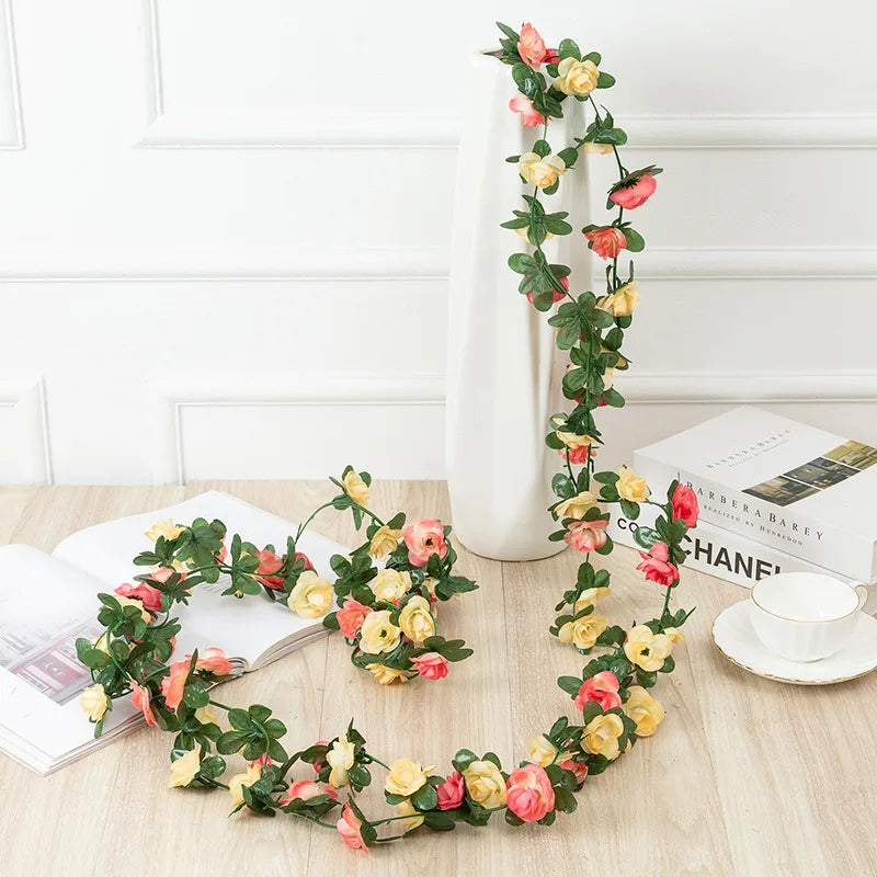 A silk rose garland featuring pink and yellow roses draped on a white vase and laid out on a wooden surface.
